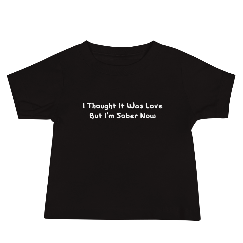"I thought it was love but I’m sober now" printed on a black baby jersey short sleeve tee laying on a flat surface