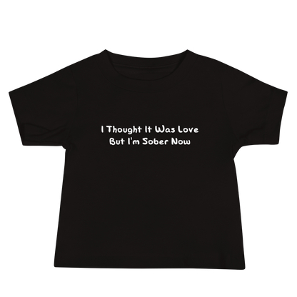 "I thought it was love but I’m sober now" printed on a black baby jersey short sleeve tee laying on a flat surface
