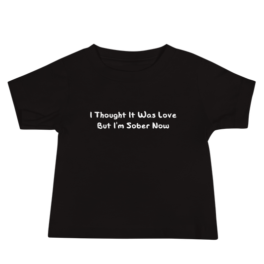 "I thought it was love but I’m sober now" printed on a black baby jersey short sleeve tee laying on a flat surface