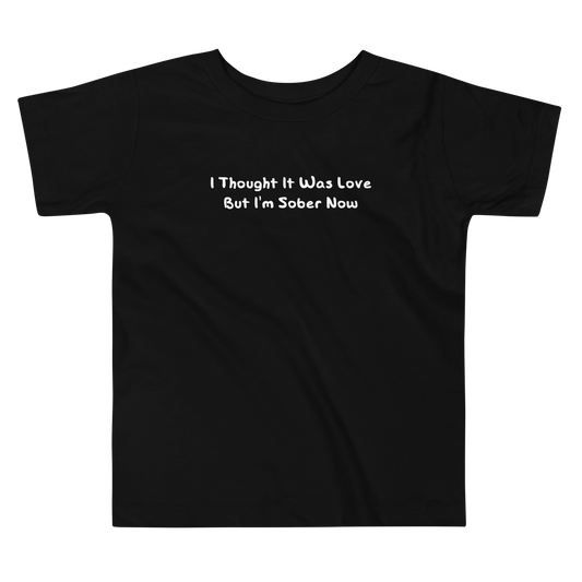 "I thought it was love but I’m sober now" printed on a black toddler short sleeve tee laying on a flat surface