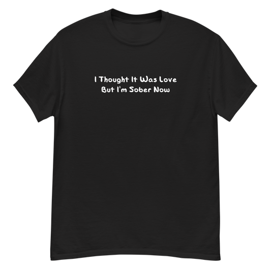 "I thought it was love but I’m sober now" printed on a black unisex classic tee laying on a flat surface