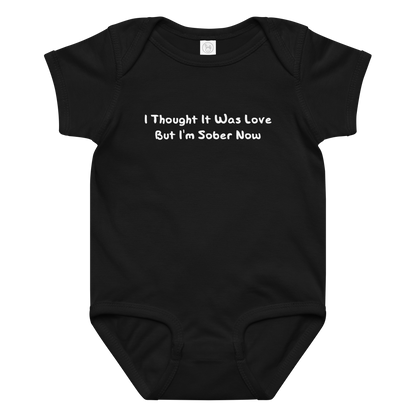 "I thought it was love but I’m sober now" printed on a black baby jersey bodysuit laying on a flat surface amongst other clothes