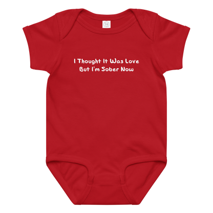 "I thought it was love but I’m sober now" printed on a red baby jersey bodysuit laying on a flat surface amongst other clothes