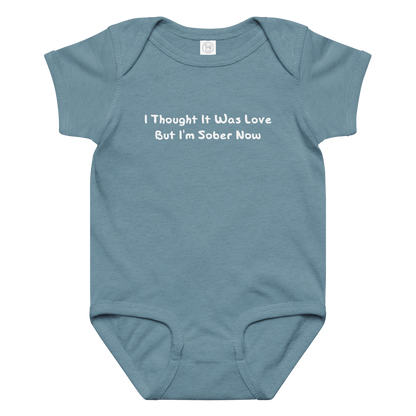 "I thought it was love but I’m sober now" printed on a vintage indigo baby jersey bodysuit laying on a flat surface amongst other clothes