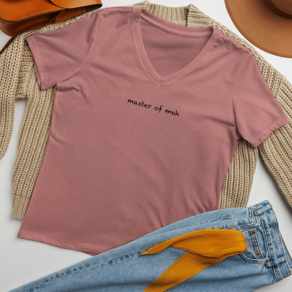 "Master of meh" printed on a heather mauve women's relaxed v-neck t-shirt laying on a flat surface amongst other clothes