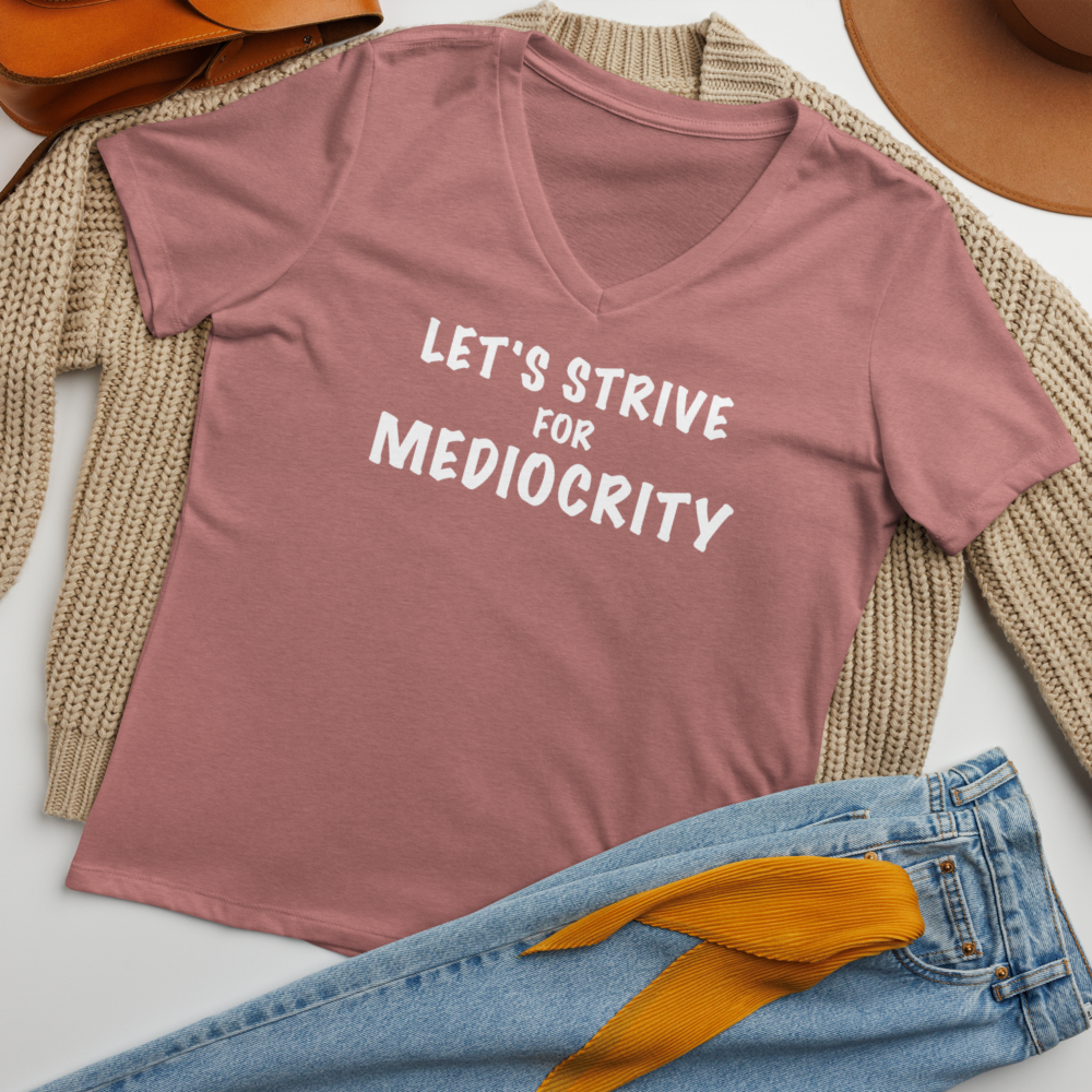 "Let's strive for mediocity" printed on a heather mauve women's relaxed v-neck t-shirt laying on a flat surface amongst other clothes