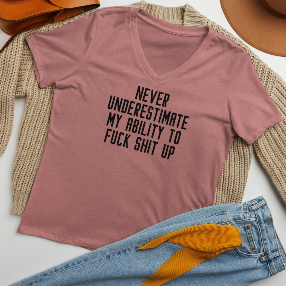 "Never Understimate My Ability To Fuck Shit Up" printed on a heather mauve women's relaxed v-neck t-shirt laying on a flat surface amongst other clothes
