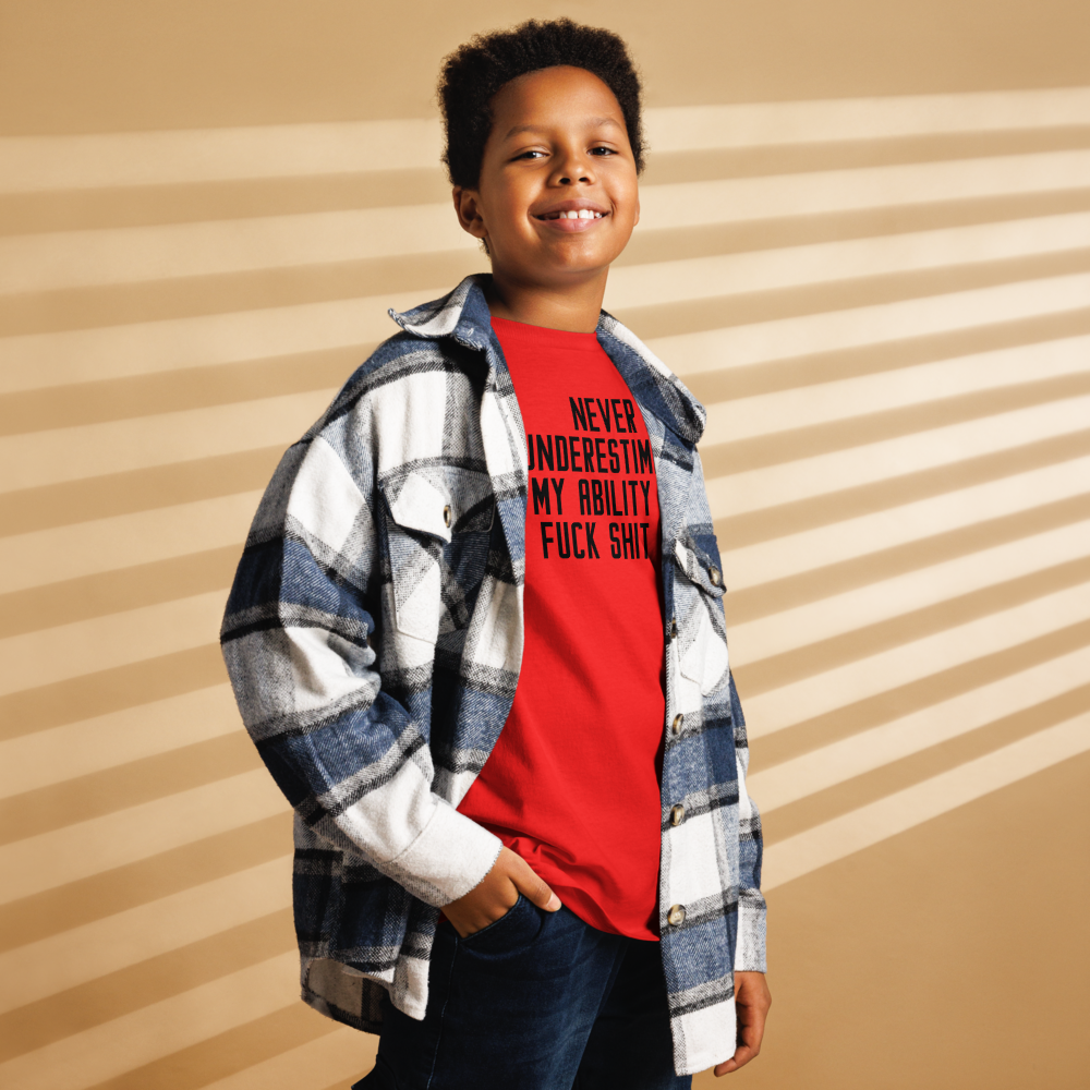 "Never Understimate My Ability To Fuck Shit Up" printed on a red youth classic tee worn by a male also wearing a jacket