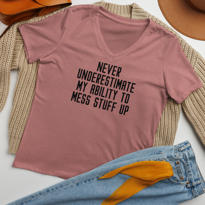 "Never Understimate My Ability To Mess Stuff Up" printed on a heather mauve women's relaxed v-neck t-shirt laying on a flat surface amongst other clothes