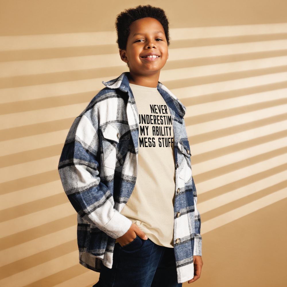 "Never Understimate My Ability To Mess Stuff Up" printed on a natural youth classic tee worn by a male also wearing a jacket