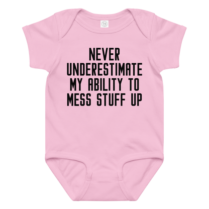 "Never Understimate My Ability To Mess Stuff Up" printed on a pink baby jersey bodysuit laying on a flat surface amongst other clothes
