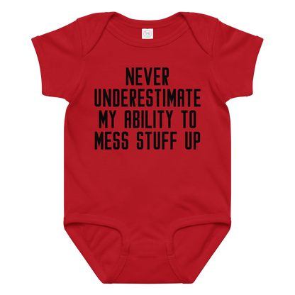 "Never Understimate My Ability To Mess Stuff Up" printed on a red baby jersey bodysuit laying on a flat surface amongst other clothes