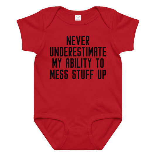 "Never Understimate My Ability To Mess Stuff Up" printed on a red baby jersey bodysuit laying on a flat surface amongst other clothes