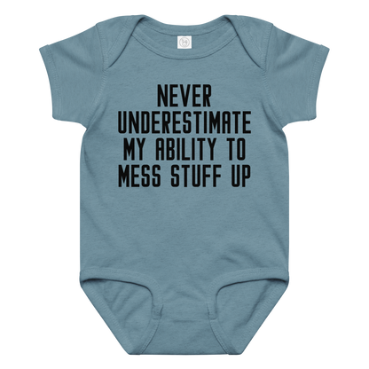"Never Understimate My Ability To Mess Stuff Up" printed on a vintage indigo baby jersey bodysuit laying on a flat surface amongst other clothes