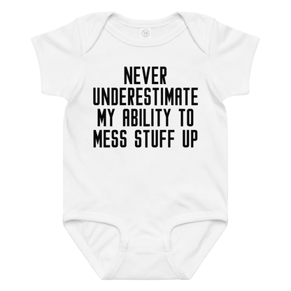 "Never Understimate My Ability To Mess Stuff Up" printed on a white baby jersey bodysuit laying on a flat surface amongst other clothes