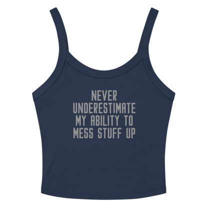 "Never Understimate My Ability To Mess Stuff Up" printed on a solid navy blend women's micro-rib tanktop laying on a flat surface amongst sunglasses and shorts