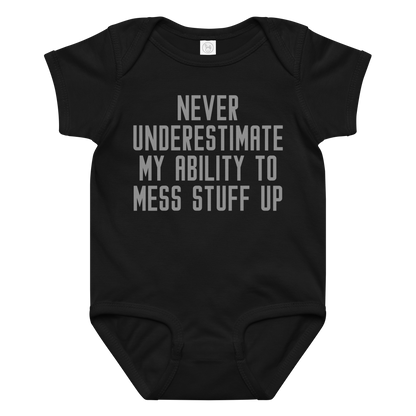 "Never Understimate My Ability To Mess Stuff Up" printed on a black baby jersey bodysuit laying on a flat surface amongst other clothes