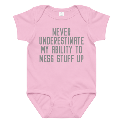 "Never Understimate My Ability To Mess Stuff Up" printed on a pink baby jersey bodysuit laying on a flat surface amongst other clothes