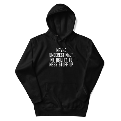 "Never Understimate My Ability To Mess Stuff Up" printed on a black unisex hoodie laying on a flat surface with the hood up