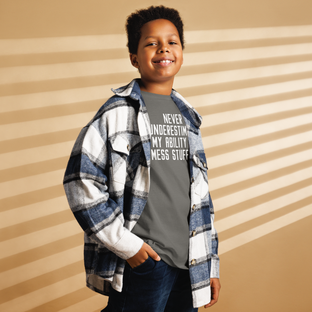 "Never Understimate My Ability To Mess Stuff Up" printed on a charcoal youth classic tee worn by a male also wearing a jacket