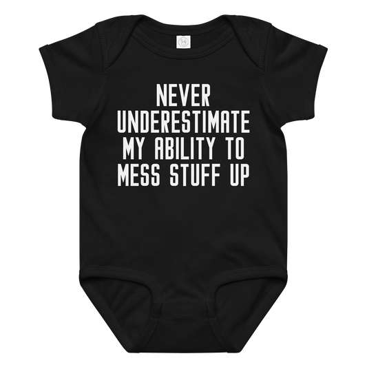 "Never Understimate My Ability To Mess Stuff Up" printed on a black baby jersey bodysuit laying on a flat surface amongst other clothes