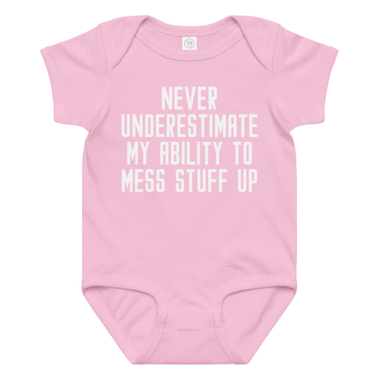 "Never Understimate My Ability To Mess Stuff Up" printed on a pink baby jersey bodysuit laying on a flat surface amongst other clothes