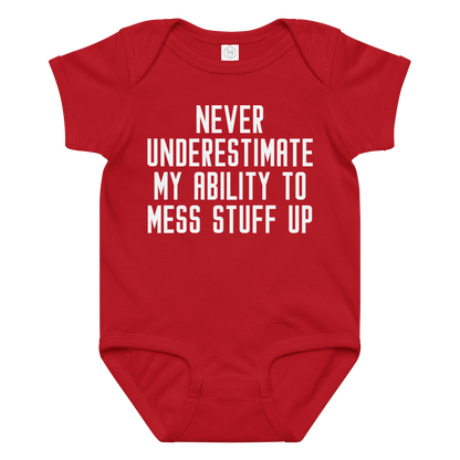 "Never Understimate My Ability To Mess Stuff Up" printed on a red baby jersey bodysuit laying on a flat surface amongst other clothes
