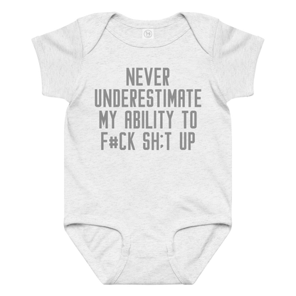 "Never Understimate My Ability To F#Ck Sh:t Up" printed on a ash baby jersey bodysuit laying on a flat surface amongst other clothes