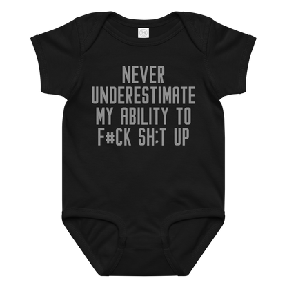 "Never Understimate My Ability To F#Ck Sh:t Up" printed on a black baby jersey bodysuit laying on a flat surface amongst other clothes