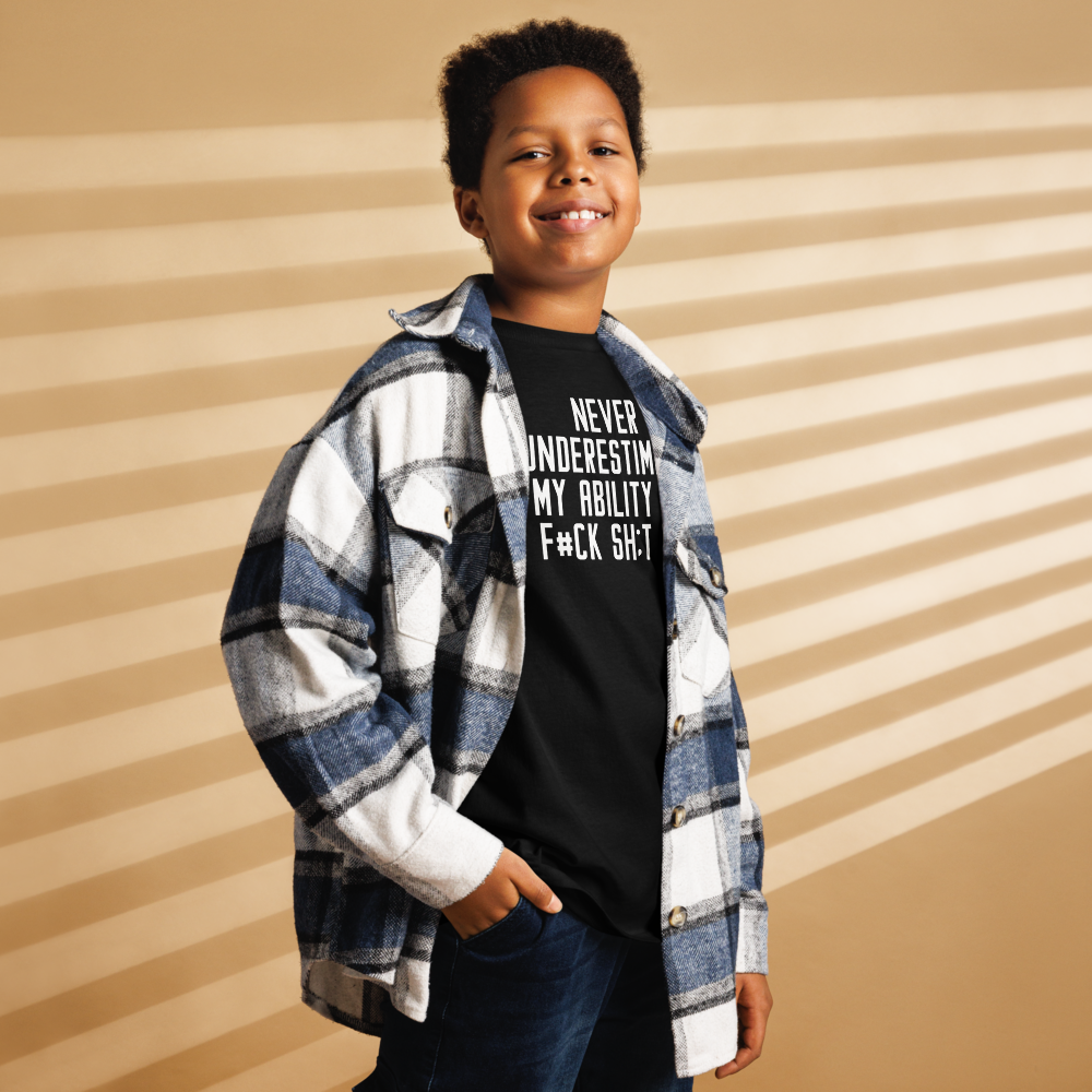 "Never Understimate My Ability To F#Ck Sh:t Up" printed on a black youth classic tee worn by a male also wearing a jacket