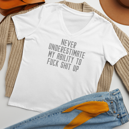 "Never Understimate My Ability To Fuck Shit Up" printed on a solid white blend women's relaxed v-neck t-shirt laying on a flat surface amongst other clothes
