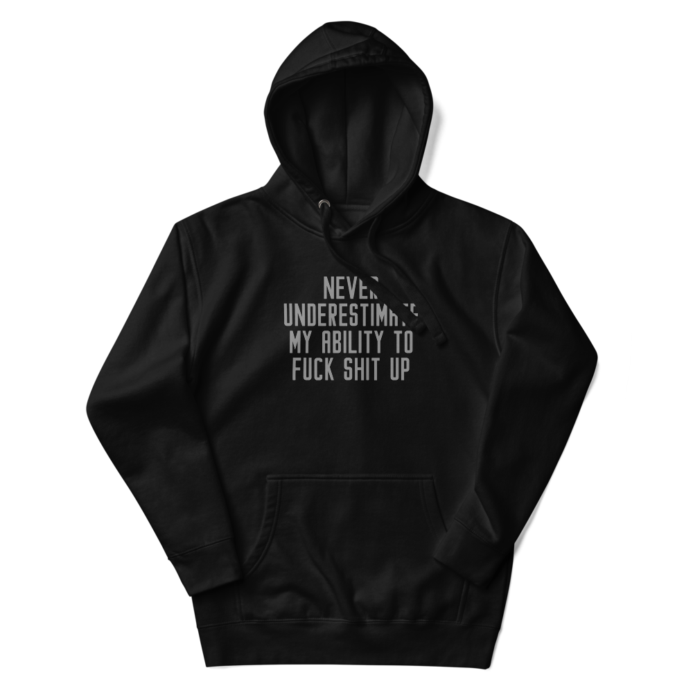 "Never Understimate My Ability To Fuck Shit Up" printed on a black unisex hoodie laying on a flat surface with the hood up