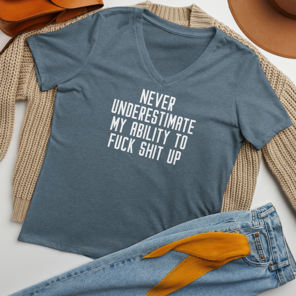 "Never Understimate My Ability To Fuck Shit Up" printed on a heather slate women's relaxed v-neck t-shirt laying on a flat surface amongst other clothes