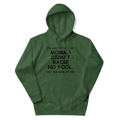 "I'd like to say that momma didn't raise no fool, but she kind of did" printed on a forest green unisex hoodie laying on a flat surface with the hood up