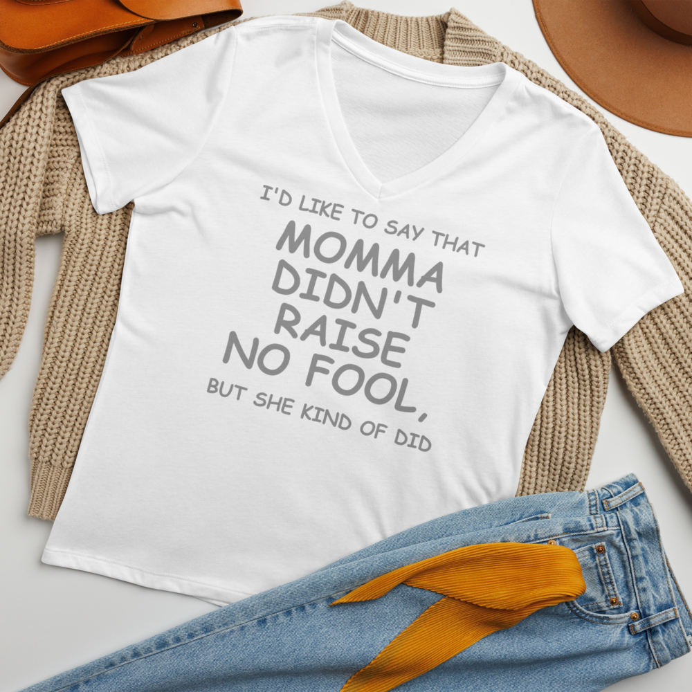 "I'd like to say that momma didn't raise no fool, but she kind of did" printed on a solid white blend women's relaxed v-neck t-shirt laying on a flat surface amongst other clothes
