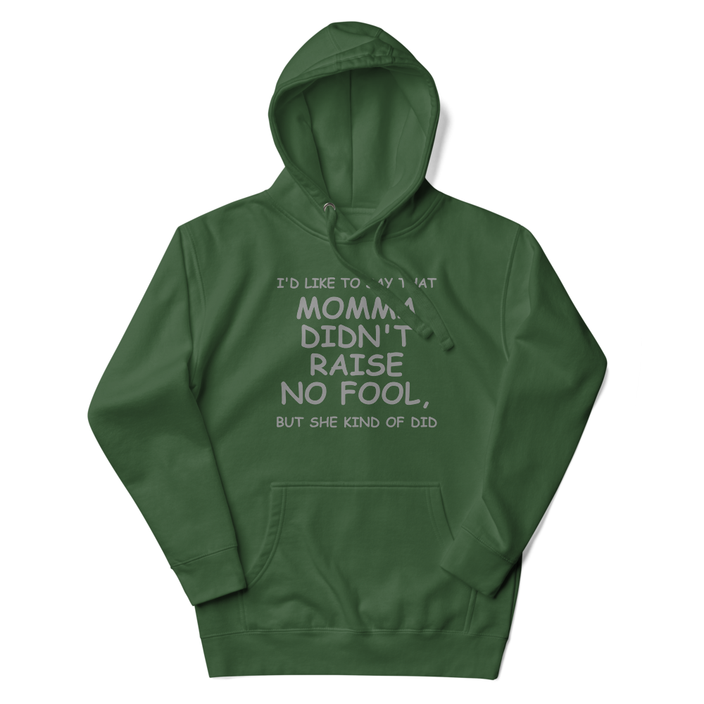 "I'd like to say that momma didn't raise no fool, but she kind of did" printed on a forest green unisex hoodie laying on a flat surface with the hood up