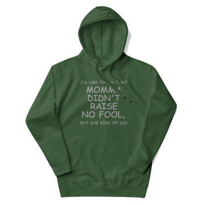 "I'd like to say that momma didn't raise no fool, but she kind of did" printed on a forest green unisex hoodie laying on a flat surface with the hood up