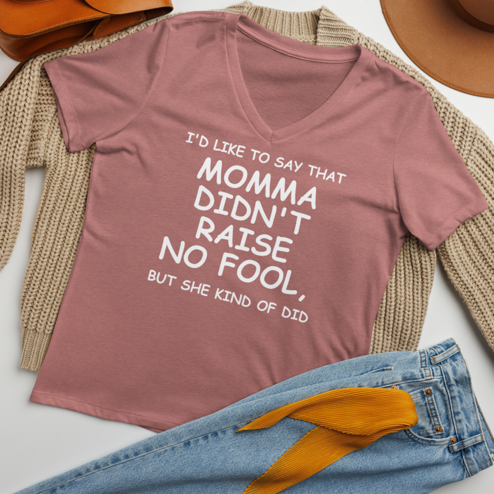 "I'd like to say that momma didn't raise no fool, but she kind of did" printed on a heather mauve women's relaxed v-neck t-shirt laying on a flat surface amongst other clothes