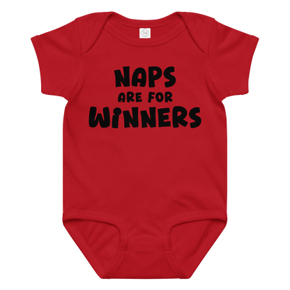 "Naps Are For Winners" printed on a red baby jersey bodysuit laying on a flat surface amongst other clothes