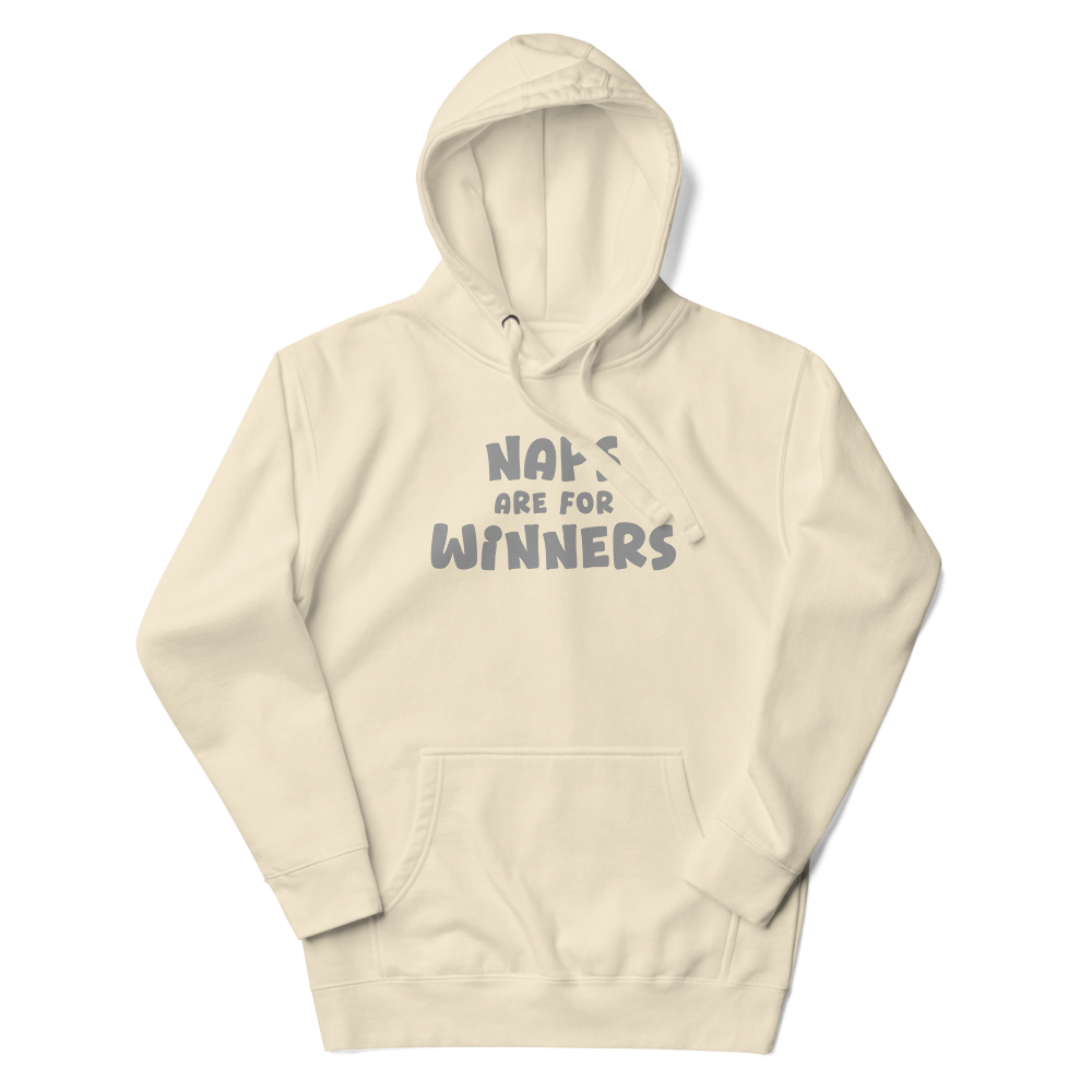"Naps Are For Winners" printed on a bone unisex hoodie laying on a flat surface with the hood up