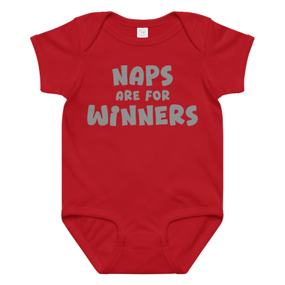 "Naps Are For Winners" printed on a red baby jersey bodysuit laying on a flat surface amongst other clothes