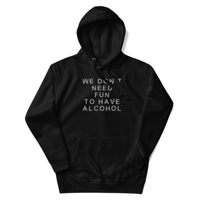 "We don’t need fun to have alcohol" printed on a black unisex hoodie laying on a flat surface with the hood up