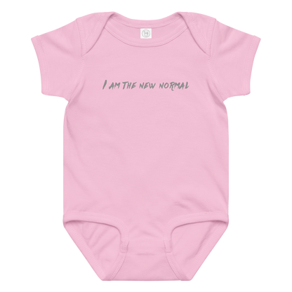 "I am the new normal" printed on a pink baby jersey bodysuit laying on a flat surface amongst other clothes