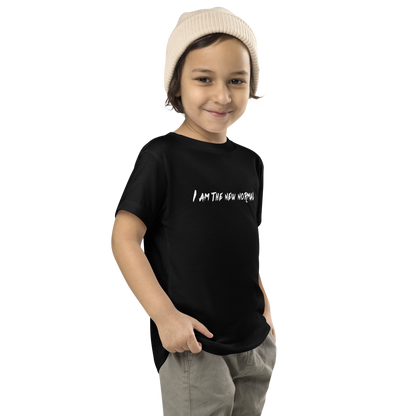 "I am the new normal" printed on a black toddler short sleeve tee worn by a male who is also wearing a knit cap