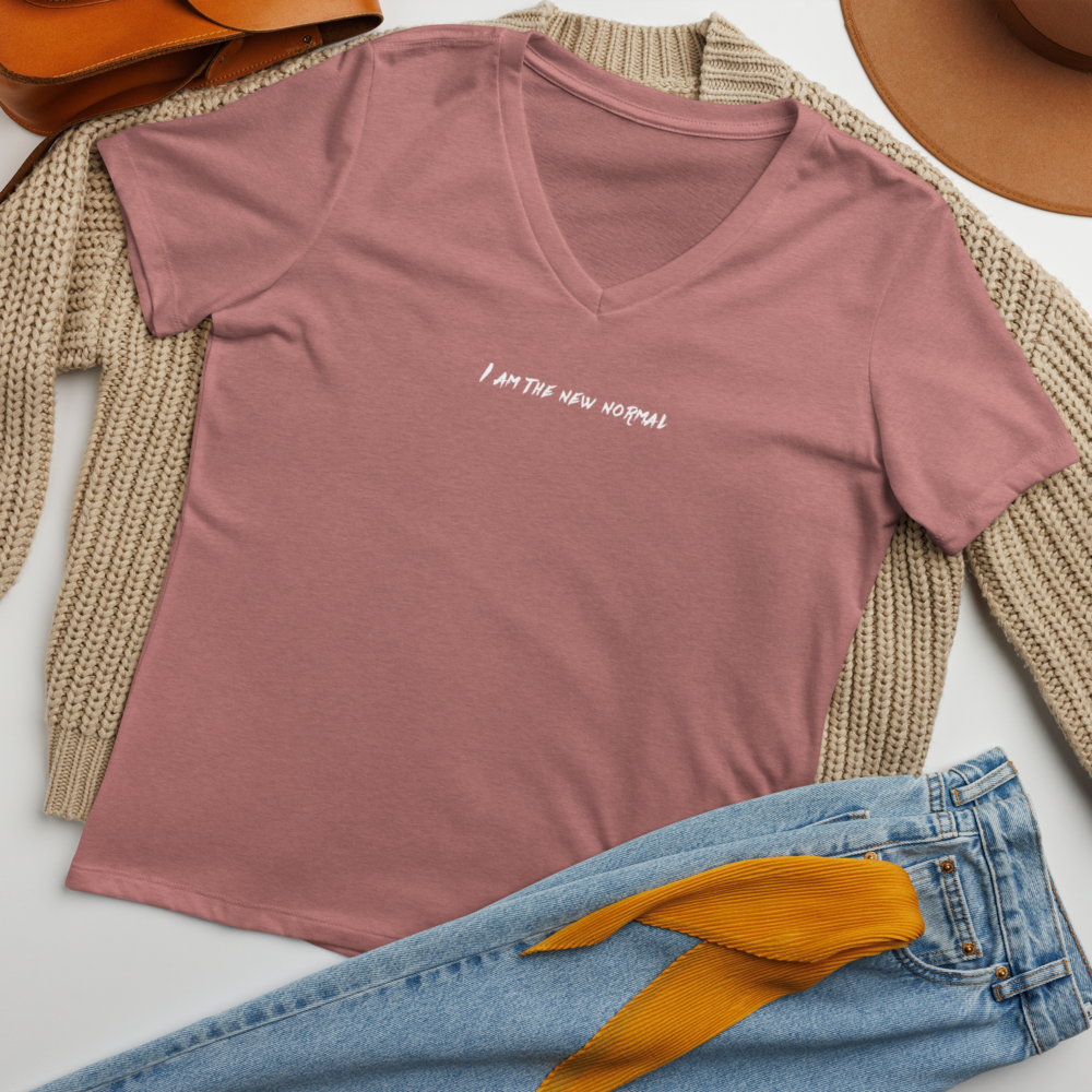 "I am the new normal" printed on a heather mauve women's relaxed v-neck t-shirt laying on a flat surface amongst other clothes