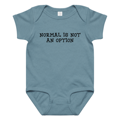 "Normal is not an option" printed on a vintage indigo baby jersey bodysuit laying on a flat surface amongst other clothes