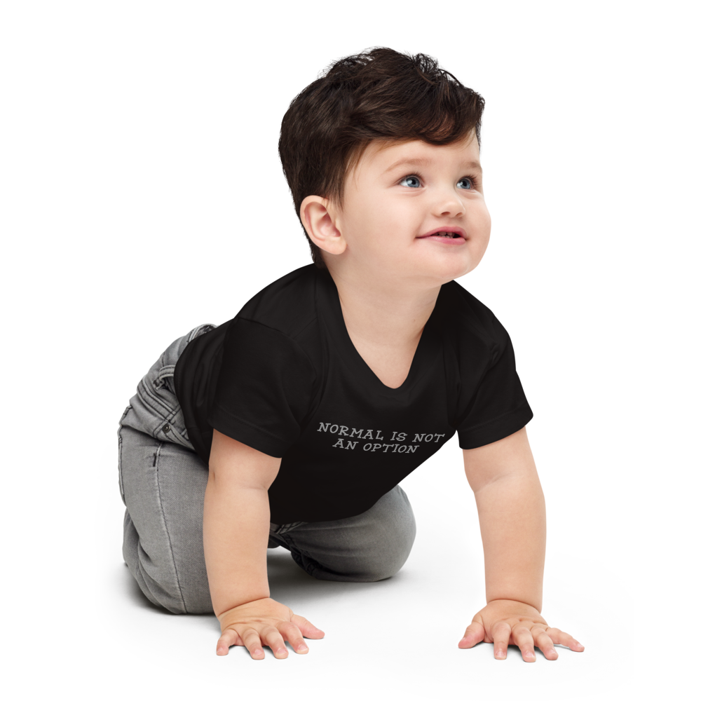 "Normal is not an option" printed on a black baby jersey short sleeve tee worn by a male who is crawling
