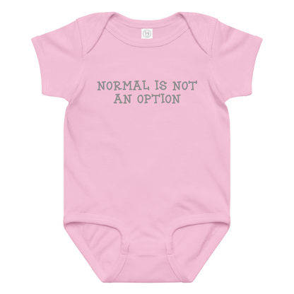 "Normal is not an option" printed on a pink baby jersey bodysuit laying on a flat surface amongst other clothes