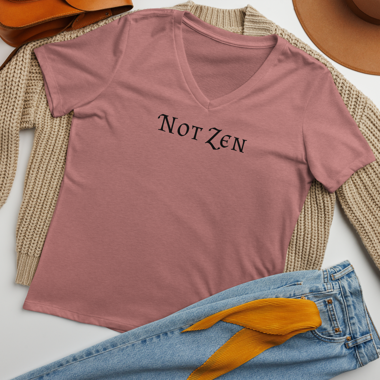 "Not zen" printed on a heather mauve women's relaxed v-neck t-shirt laying on a flat surface amongst other clothes