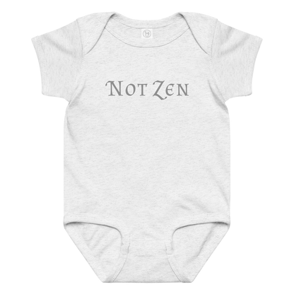 "Not zen" printed on a ash baby jersey bodysuit laying on a flat surface amongst other clothes